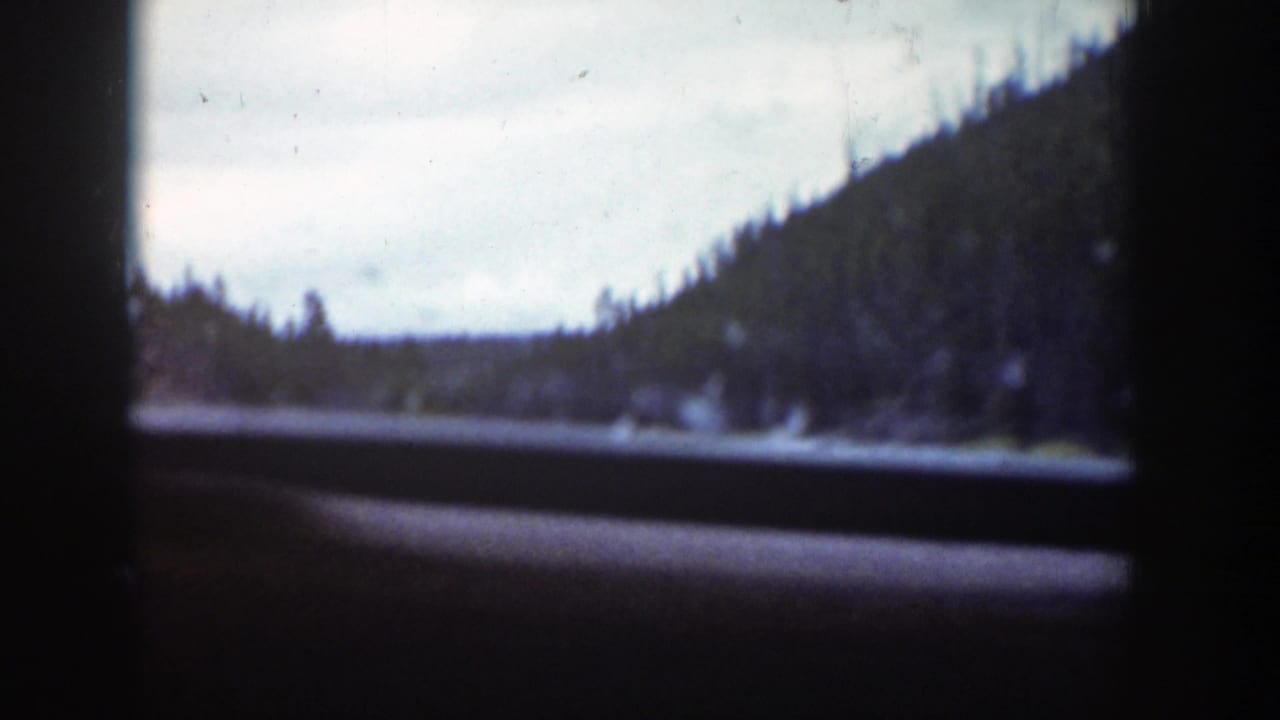 A 1939 Wyoming mountain river scene appears beyond dark car-window framing during a moving road shot.
