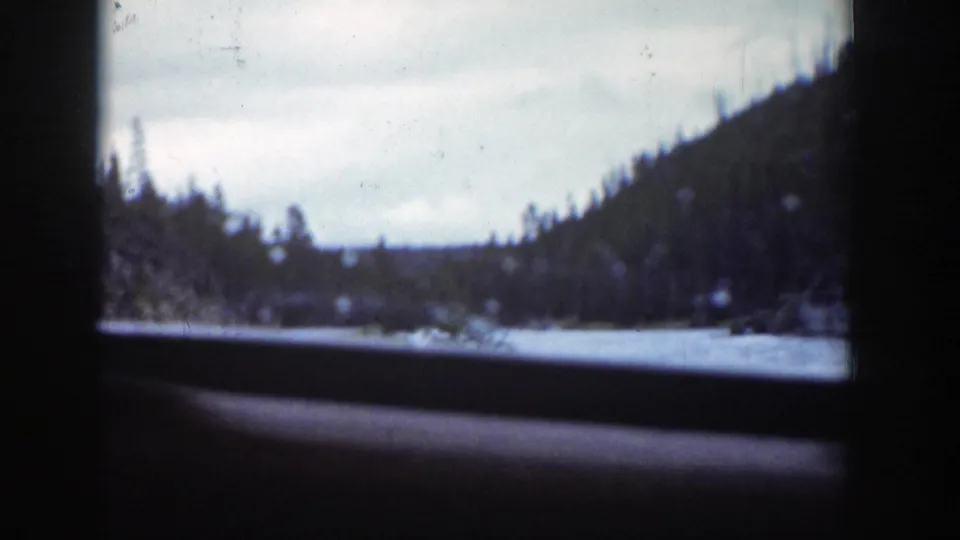 Wyoming mountain river scenery from a 1939 8mm home movie, framed by the vehicle interior and window edge.