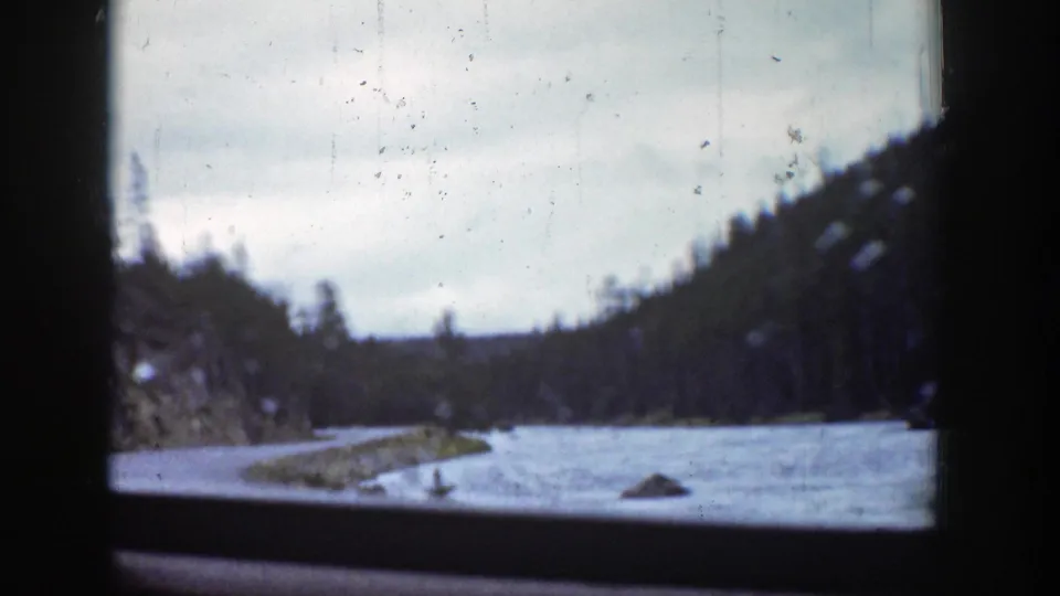 A brief 1939 Wyoming road-view frame shows a river bend, rocky shoreline, and wooded mountain slopes through the car window.