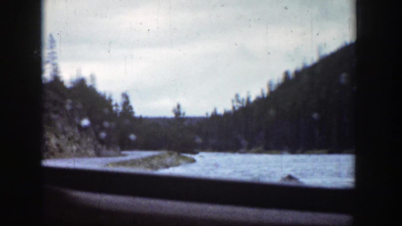 1939 Wyoming home-movie view of blue water and forested hills through a dark vehicle window frame.