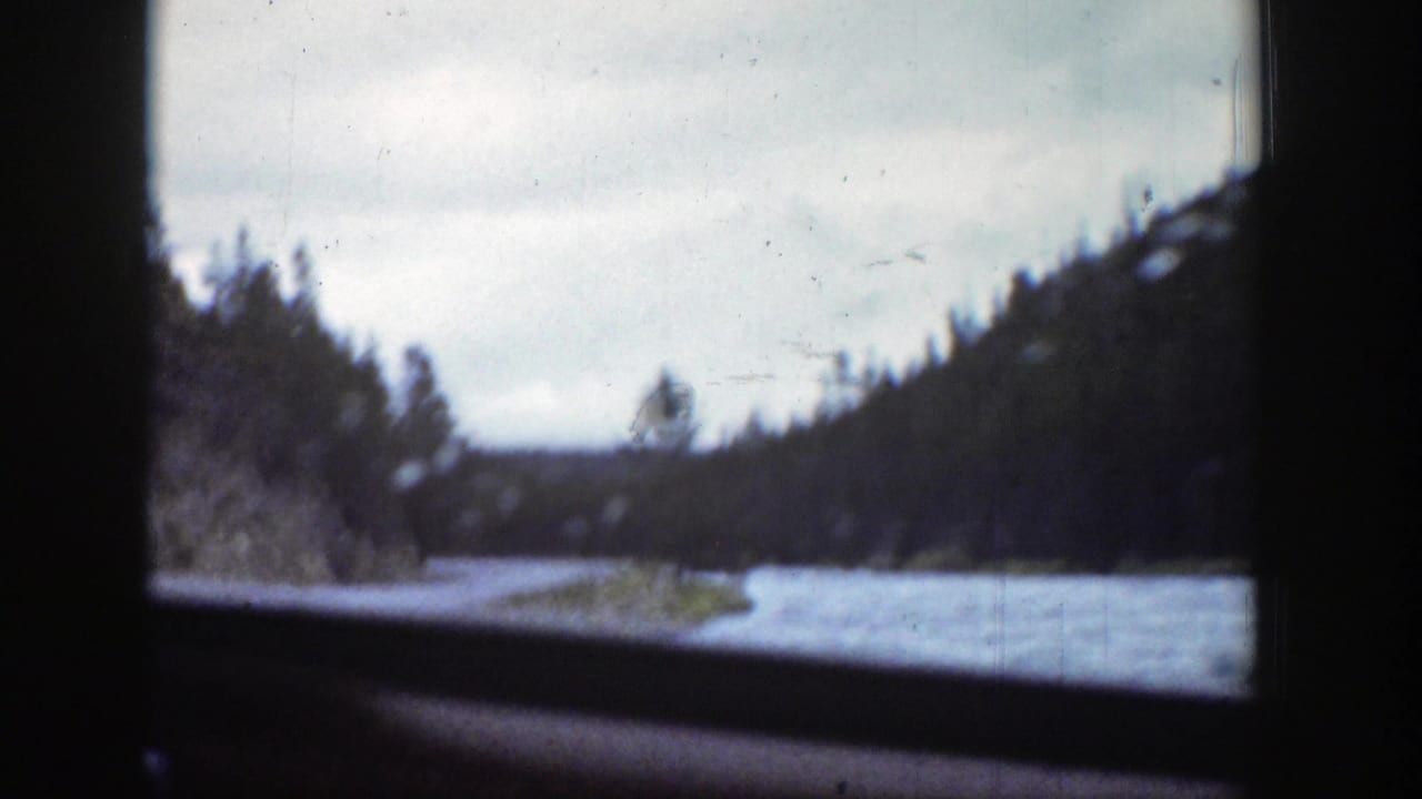 Curving waterway and wooded hillside viewed through the right side of a window.