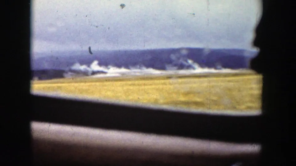 Wyoming landscape from a moving vehicle, with yellow grass, distant ridge, water, and a dark interior window edge.