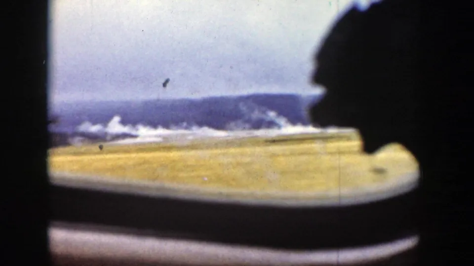 End-frame view from inside the vehicle, showing water, yellow grass, distant Wyoming hills, and a dark window-side silhouette.