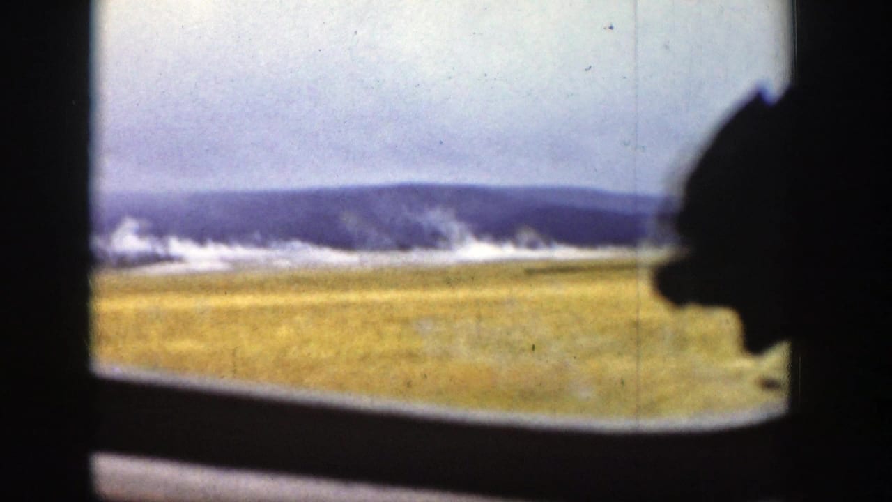 Train-window view of open fields and mountains with a dark passenger silhouette at right.