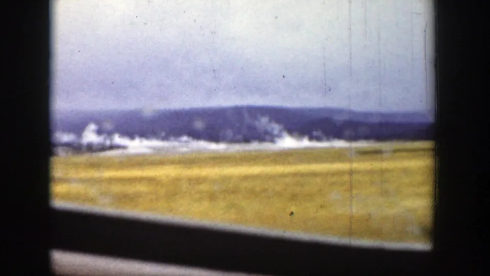 1939 Wyoming landscape seen from inside a moving train, with dark window framing, golden field, pale sky, and distant mountains.