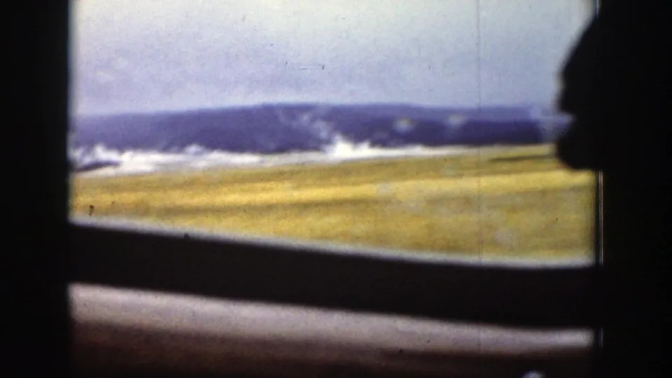 1939 Wyoming train interior view with a silhouetted passenger profile, dark window frame, open fields, and distant snowy mountains.
