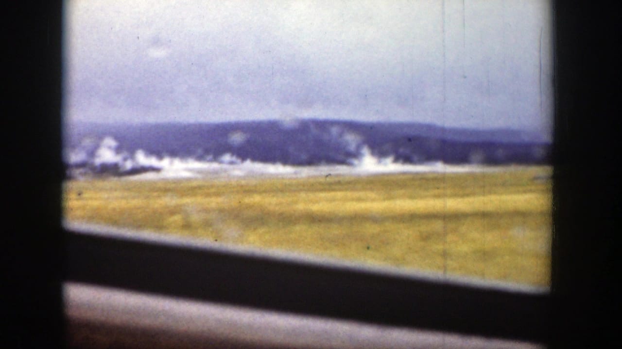 Wyoming landscape with distant hills, pale sky, yellow plain, and steam beyond a dark window or vehicle frame in 1939 8mm footage.