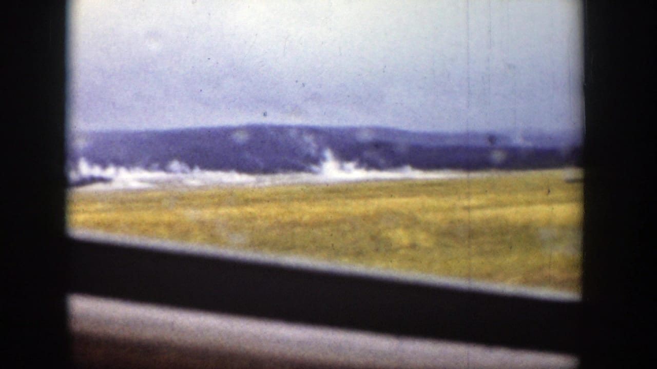 A similar Wyoming vista shows a broad plain, low mountains, pale sky, and geothermal steam framed by dark vehicle or window edges.