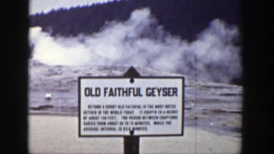 A close view of the Old Faithful Geyser sign appears before a steaming geyser basin, with dark film or vehicle framing along the edge.