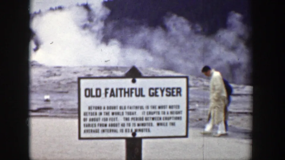 A visitor passes beside the Old Faithful Geyser sign while the geyser steam fills the background in this 1939 Wyoming footage.