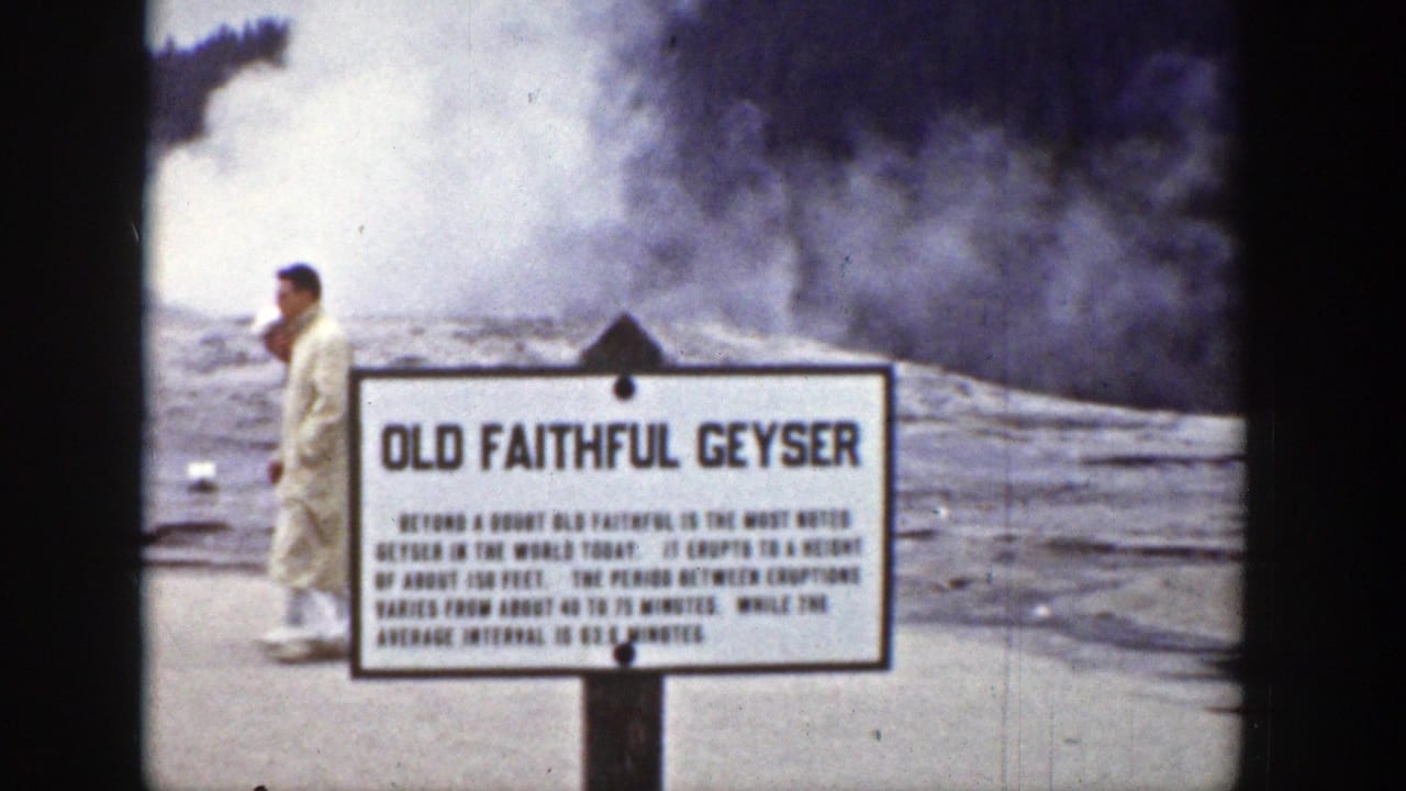 Man in a light suit walking past the Old Faithful Geyser sign during an eruption.