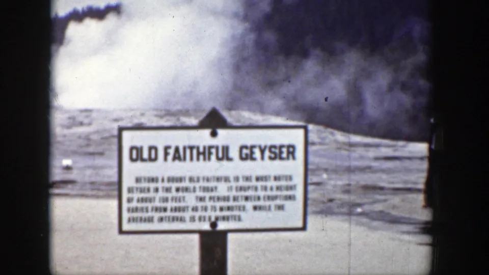 1939 Wyoming home-movie still with the Old Faithful Geyser sign centered before dense steam and a geothermal mound.