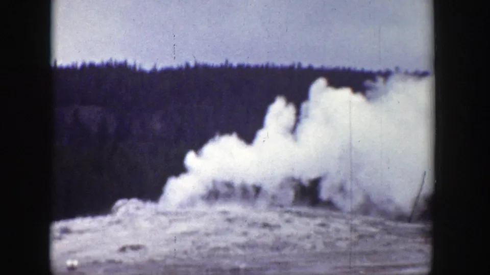 1939 Wyoming frame showing Old Faithful erupting, with a broad white plume rising in front of a dark tree line.