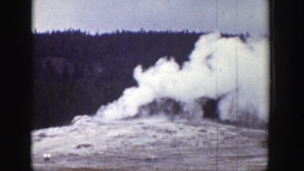 1939 Wyoming 8mm frame showing a geyser eruption beginning or receding near a conifer forest under a pale sky.