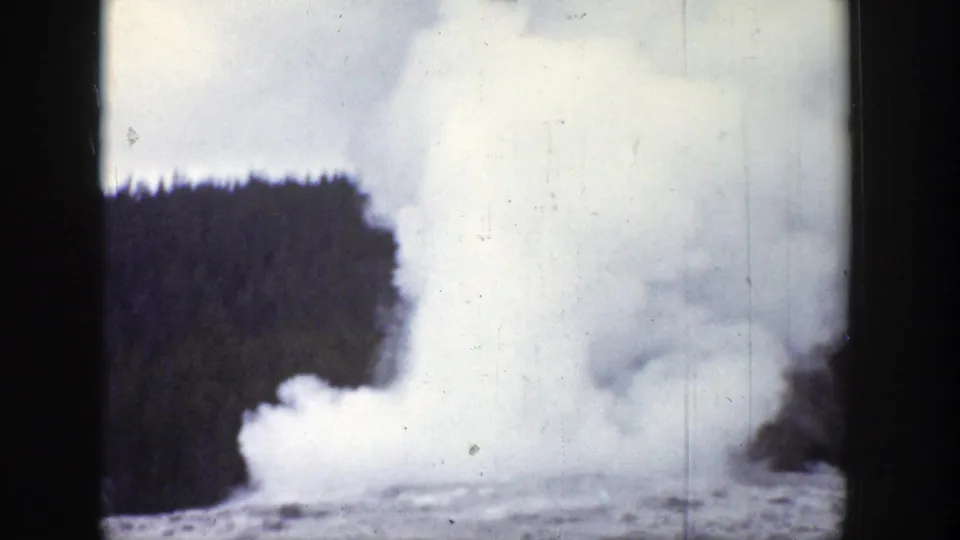 1939 Wyoming 8mm frame with a large geyser plume rising sharply near a forested backdrop.