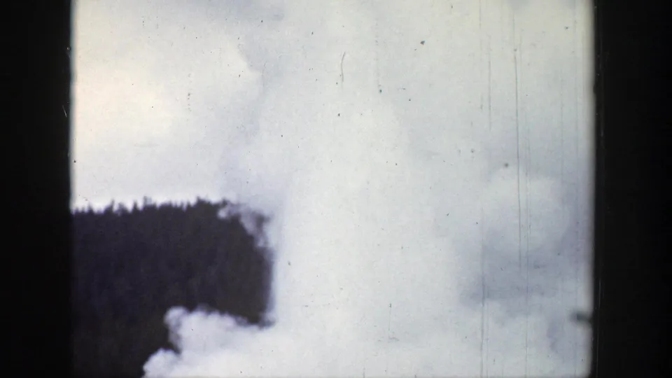 1939 Wyoming 8mm frame showing lingering geyser steam drifting beside the dark conifer forest.