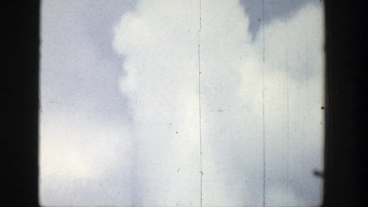 Tall smoke column against a pale sky with dark vertical frame edges.