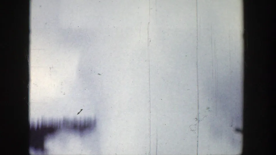 1939 Wyoming 8mm frame showing faint smoke haze across a pale sky with blurred dark tree forms near the lower edge.