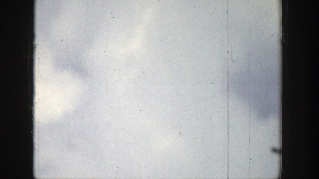 1939 Wyoming 8mm frame showing an overcast sky through a dark window edge, with dust, grain, and vertical scratches.