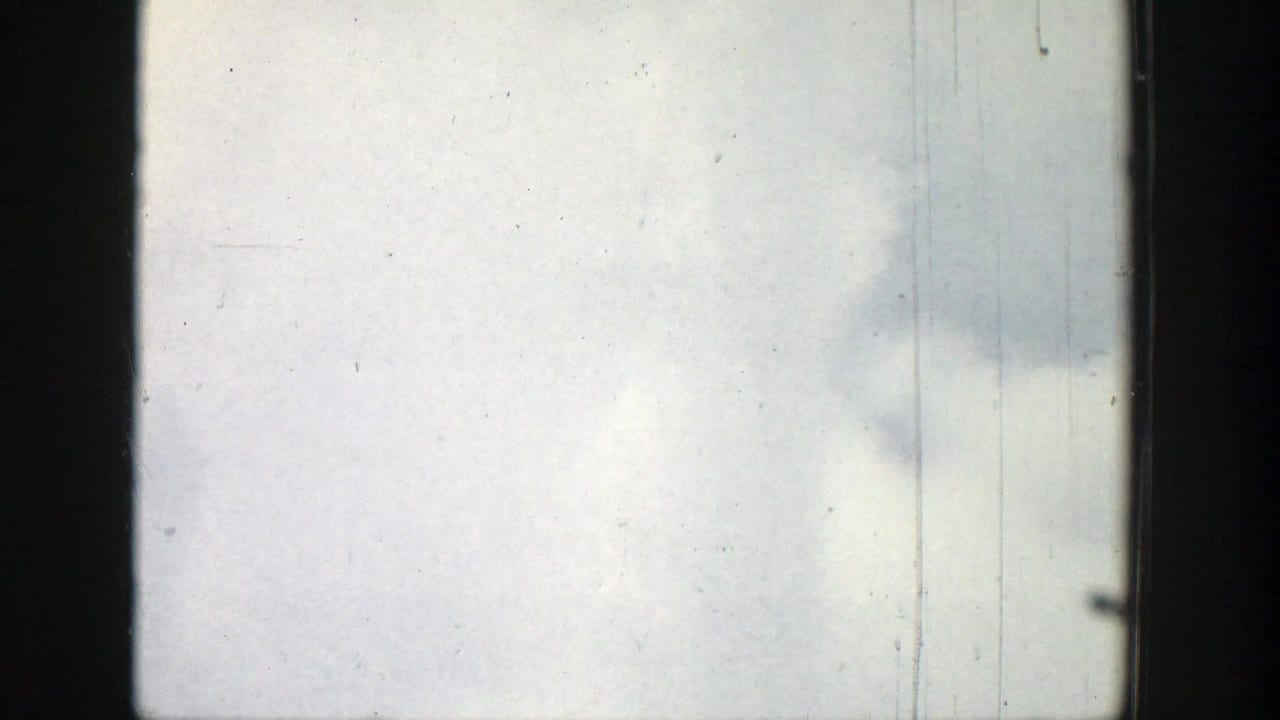 Pale cloudy sky behind dark window framing with light scratches and dust marks.