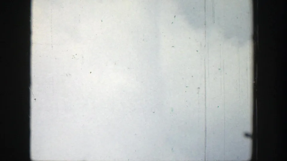 Final 1939 Wyoming 8mm frame with pale overcast sky, dark window borders, vertical scratches, dust, and slight flicker.