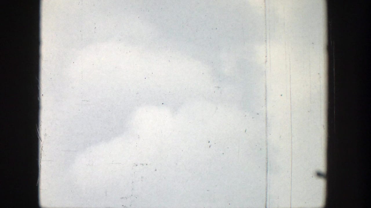 Pale clouded sky in the Wyoming home-movie footage, bordered by dark 8mm frame edges with scratches and dust marks.