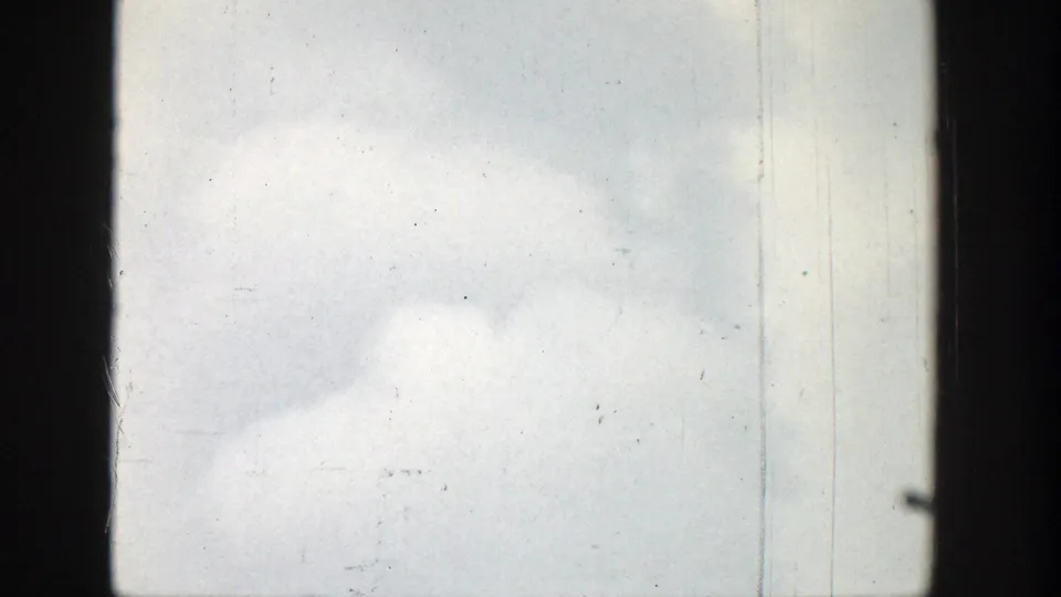 Pale clouded sky in the Wyoming home-movie footage, bordered by dark 8mm frame edges with scratches and dust marks.