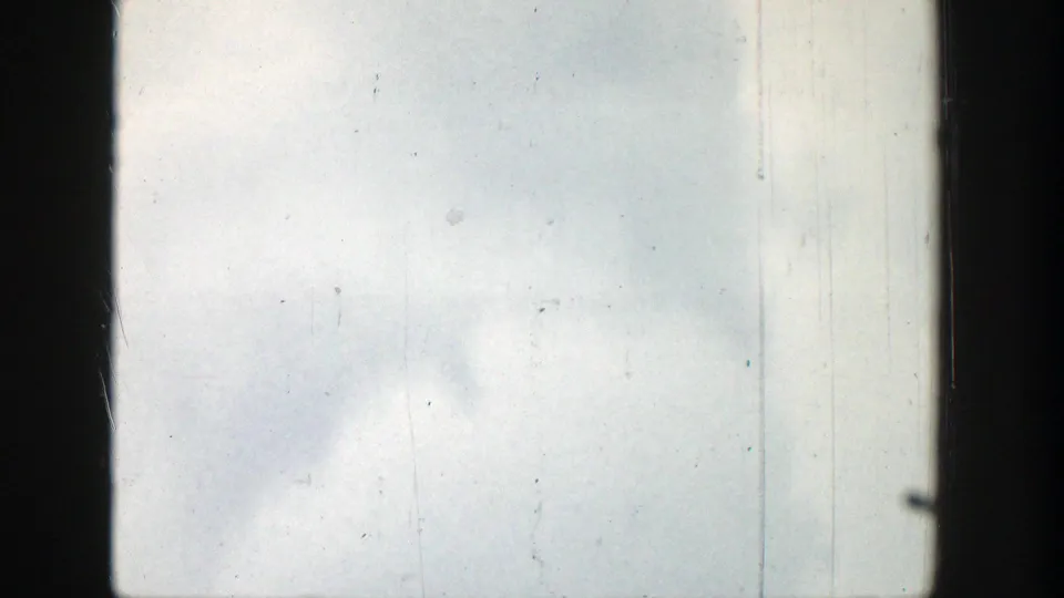 Washed-out 8mm frame from the 1939 Wyoming clip, showing pale sky, faint cloud forms, scratches, dust, and dark film edges.