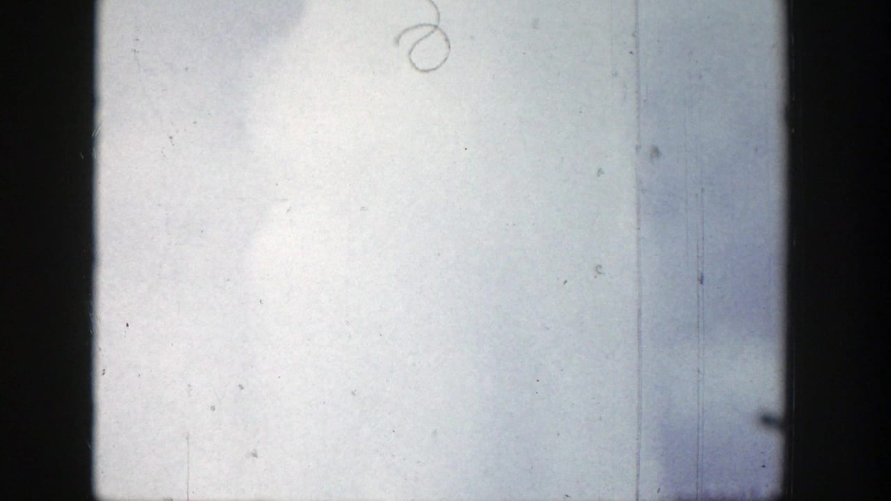 1939 Wyoming 8mm frame showing a pale sky and soft geyser vapor rising near the lower edge, with film scratches and dark frame borders.
