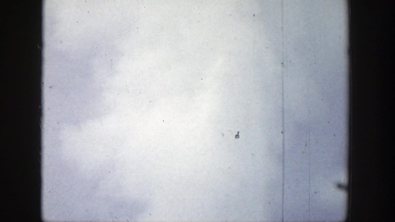 1939 Wyoming 8mm frame with pale sky, a dark vertical gate edge, and faint geyser steam near the right side.