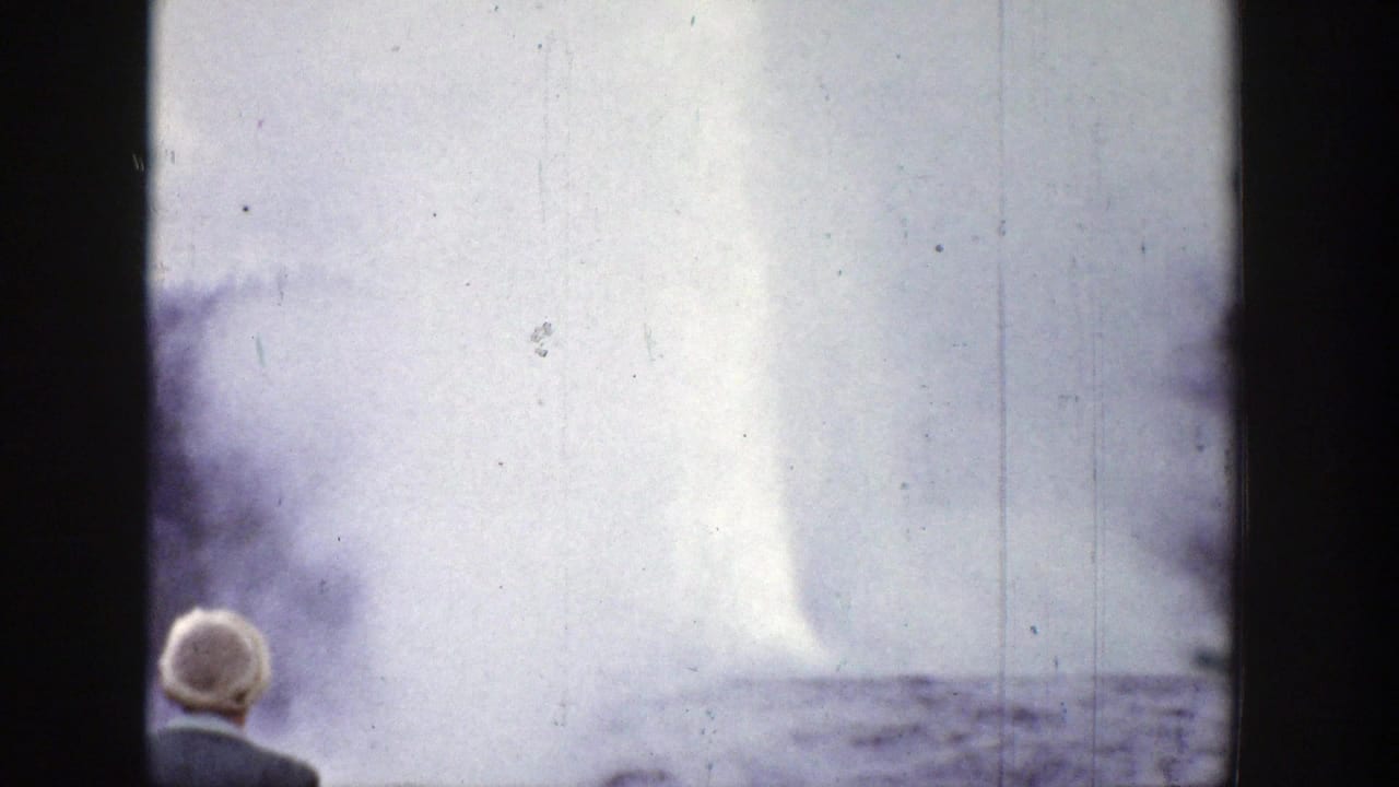 Geyser plume rising as a white-haired spectator watches from behind.