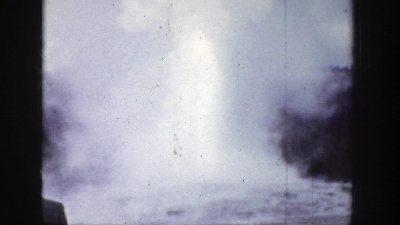 1939 Wyoming 8mm frame showing a bright geyser steam plume rising above a low basin, with dark trees and film scratches visible.