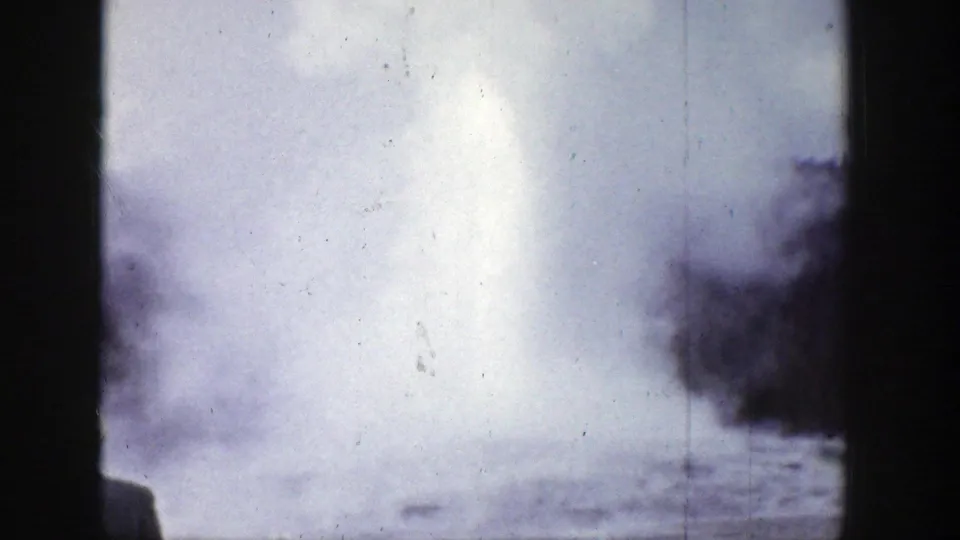 1939 Wyoming 8mm frame showing a bright geyser steam plume rising above a low basin, with dark trees and film scratches visible.