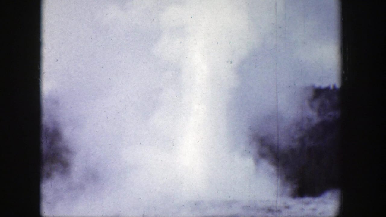 Tall geyser plume with trees at the sides and visible film wear.