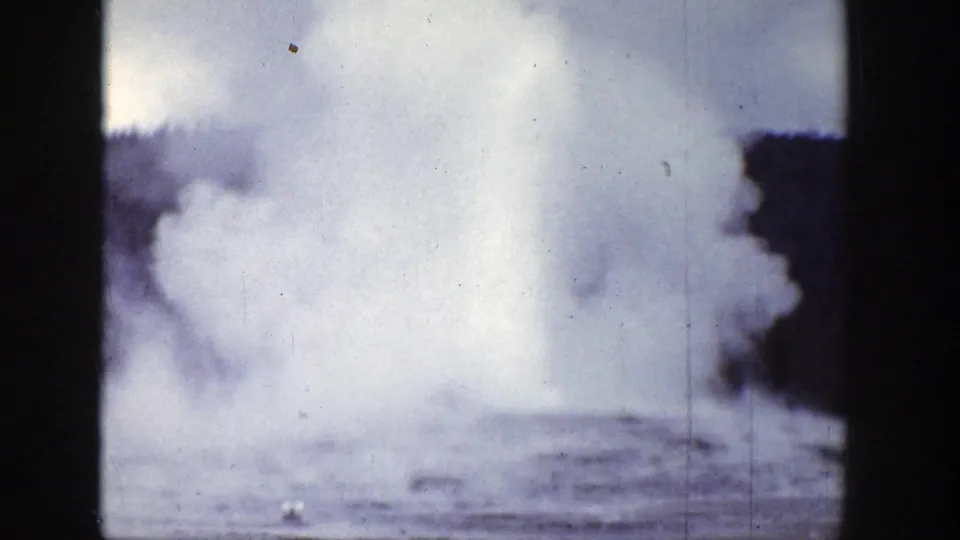 1939 Wyoming 8mm frame showing a broad geyser steam cloud over a low basin, with dark trees at the right edge and aged film texture.