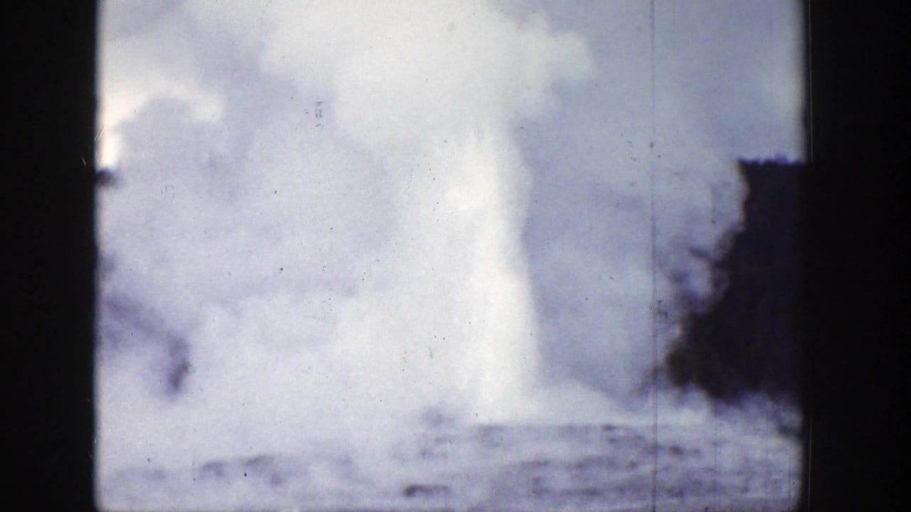 1939 Wyoming 8mm frame with a bright geyser eruption against cloudy sky and dark surrounding tree shapes.