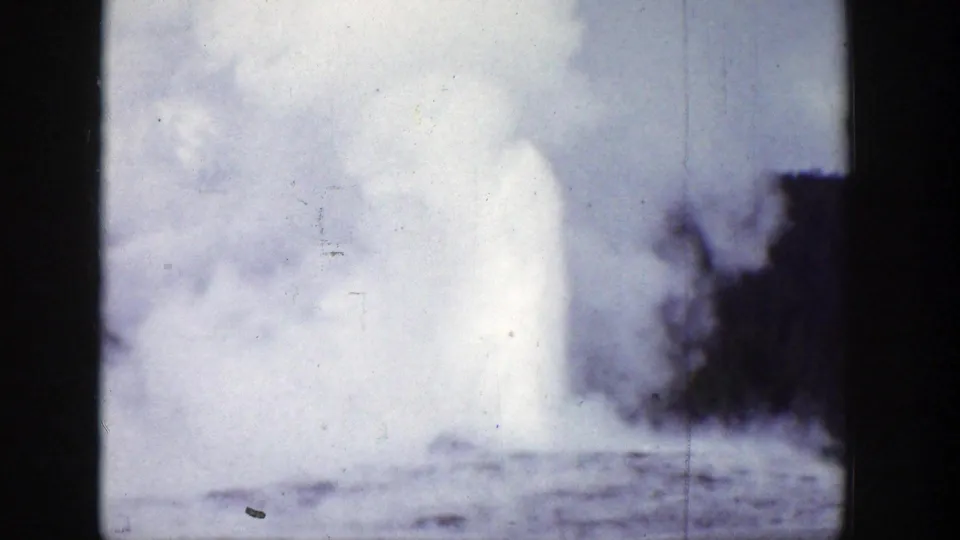Faded 1939 Wyoming 8mm frame showing a geyser plume spreading into a dense steam cloud over rough terrain.