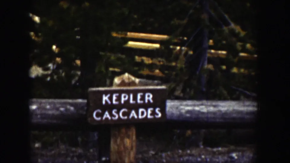 1939 Wyoming 8mm frame showing a rustic Kepler Cascades sign, log rail, and evergreen forest background.