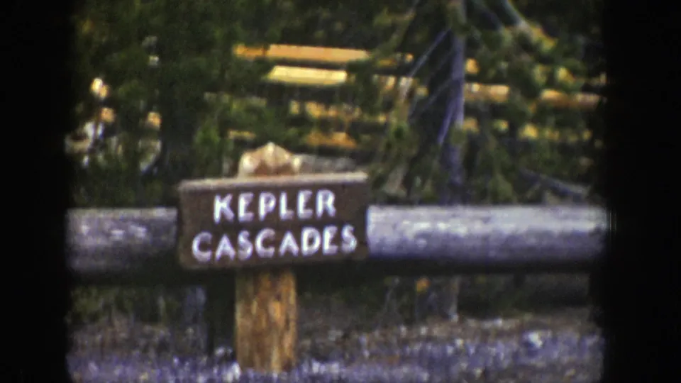 1939 Wyoming 8mm frame with a closer visitor view of the Kepler Cascades sign against forest and railings.
