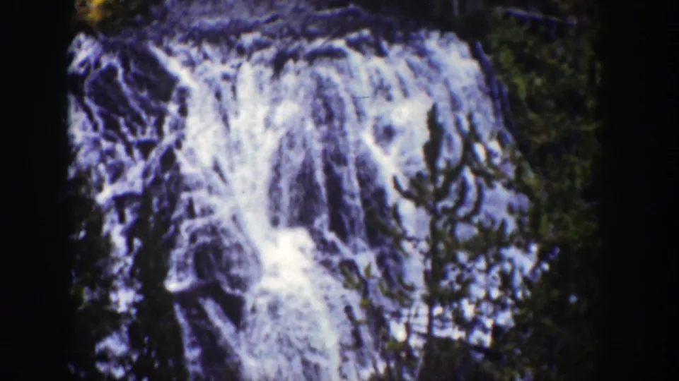 1939 Wyoming home-movie frame showing Kepler Cascades water falling over dark rocky terrain with forest at the edges.