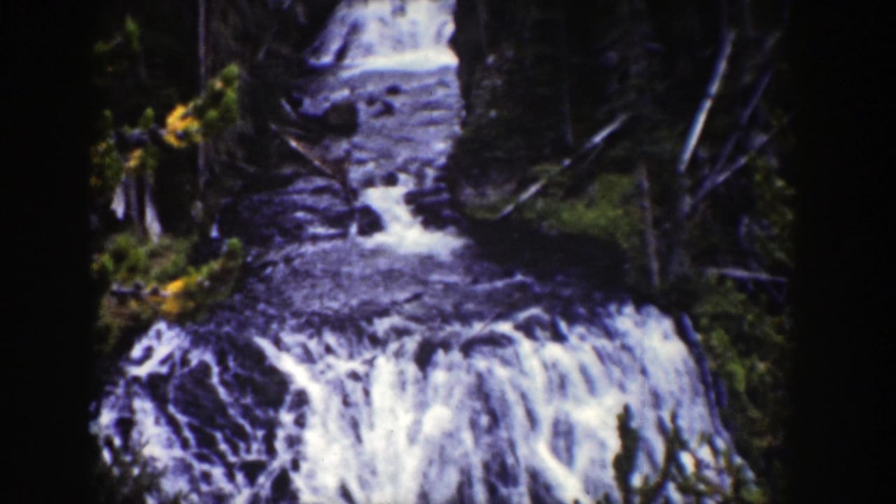 1939 Wyoming 8mm frame with a forest stream feeding a broad whitewater drop through wooded terrain.