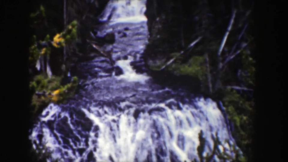 1939 Wyoming 8mm frame with a forest stream feeding a broad whitewater drop through wooded terrain.