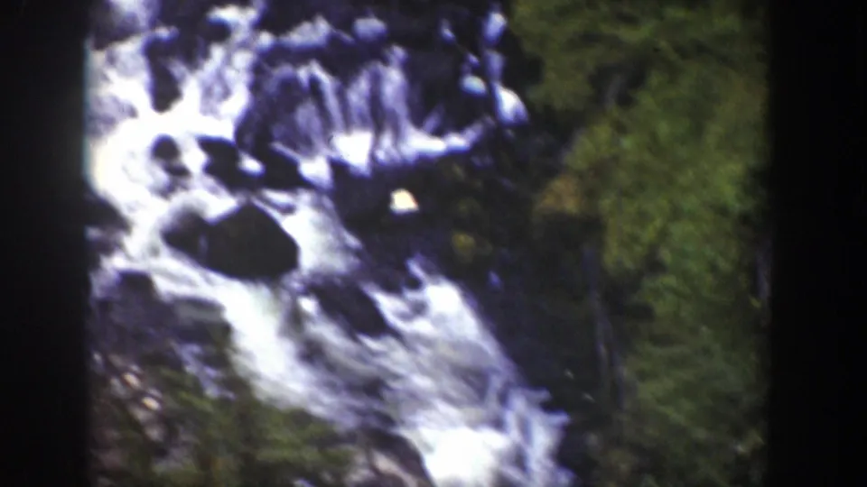 1939 Wyoming 8mm frame showing a waterfall spilling over dark boulders beside dense green forest.