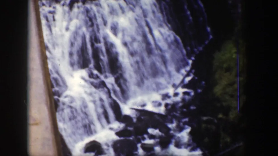 1939 Wyoming 8mm frame with a wide waterfall face, dark rocks, forest edge, and pale foreground border.