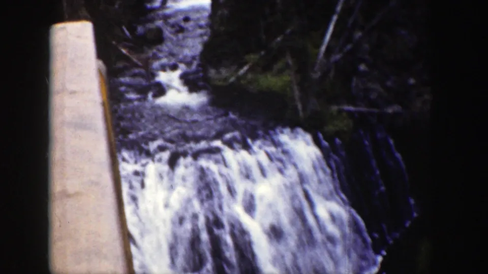 1939 Wyoming 8mm frame showing a lower waterfall section feeding a rocky stream under forest shade.