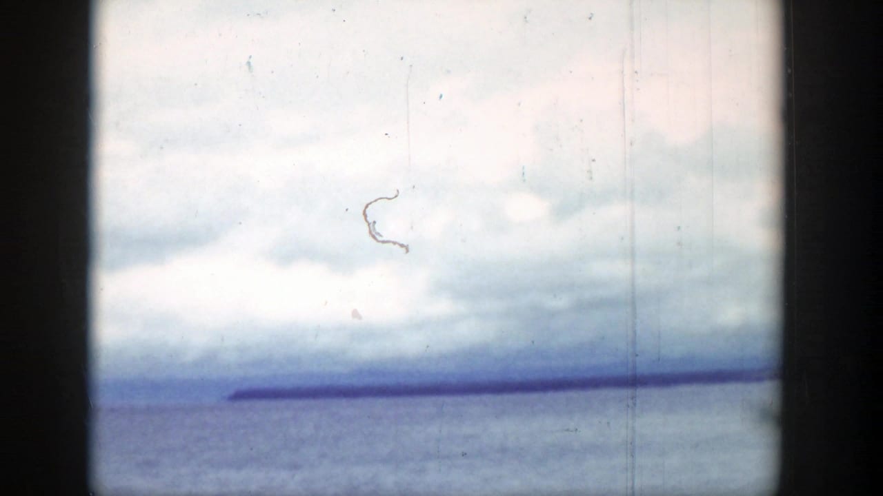 Lake and distant shoreline beneath cumulus clouds, framed by dark vertical vehicle or window edges.