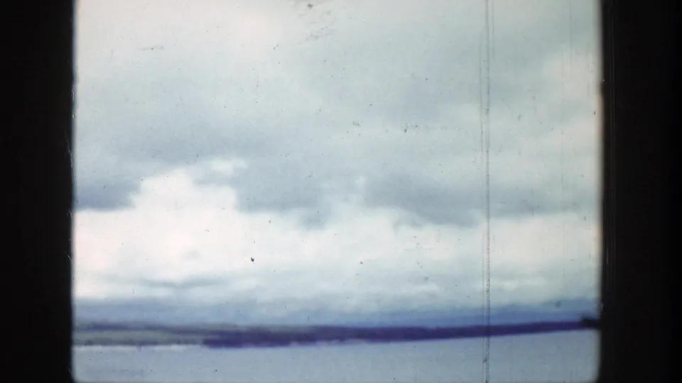 1939 Wyoming home-movie still with heavy cumulus clouds, lake water, and a narrow distant shoreline seen from a moving viewpoint.