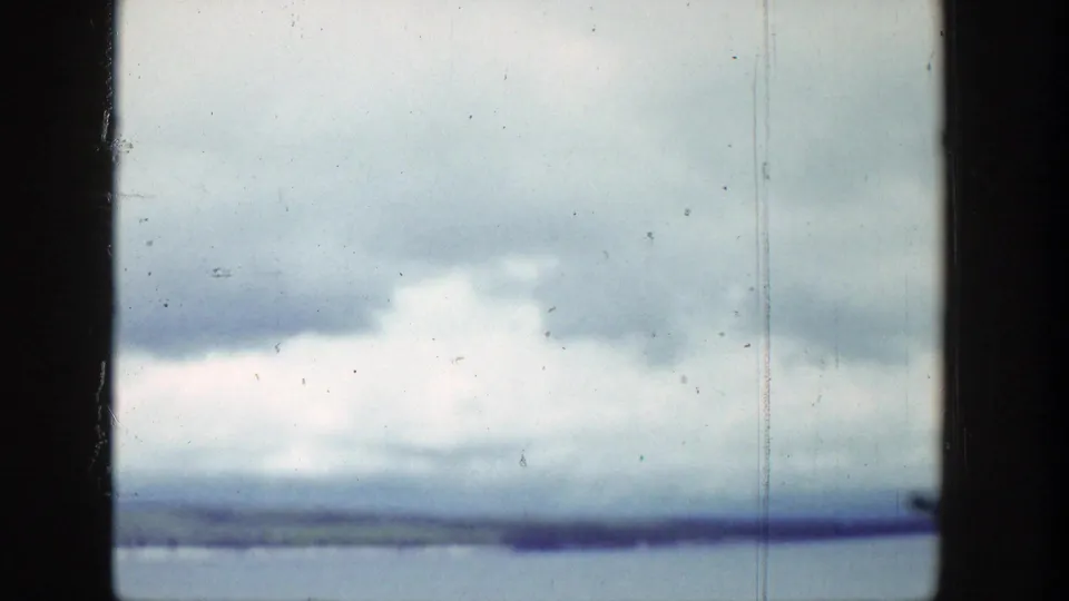 1939 Wyoming 8mm frame showing bright cumulus clouds, blue-gray lake water, and a distant shore through dark vehicle or window edges.