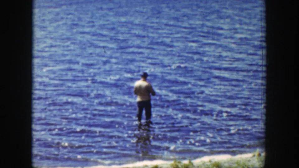 The 1939 Wyoming footage shows a distant man standing knee-deep in rippled lake water, viewed from shore.