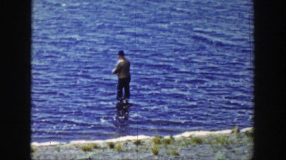 1939 Wyoming 8mm frame showing an adult man in a hat standing in rippling blue lake water near the shore.
